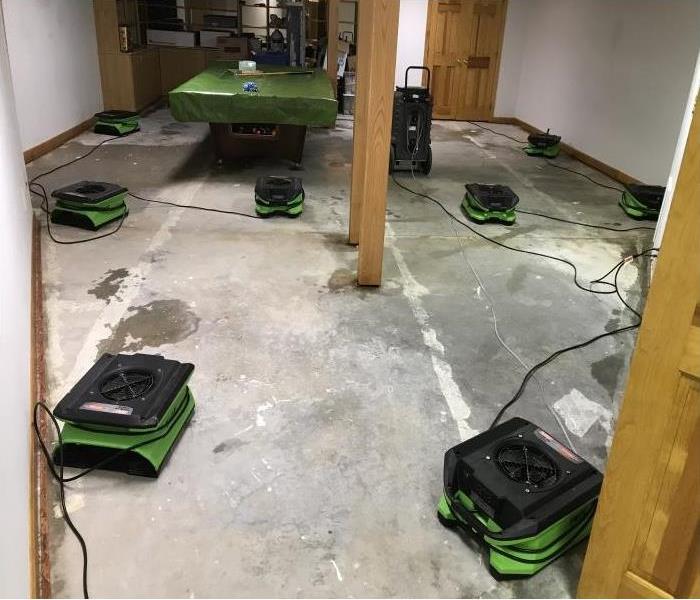Air movers and dehumidifiers being used to dry a damp basement